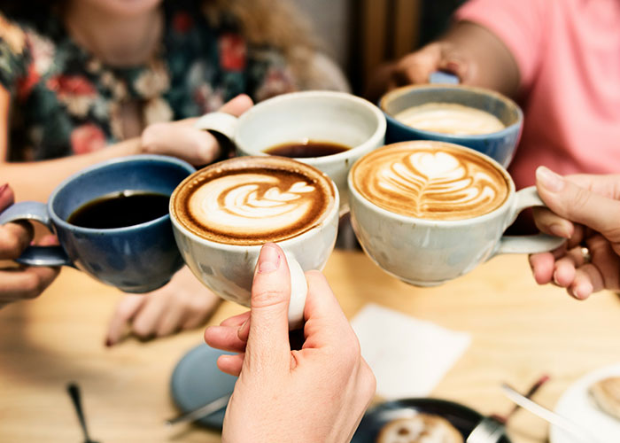 Group of people clinking coffee cups with latte art, highlighting barista and decaf revenge interaction.