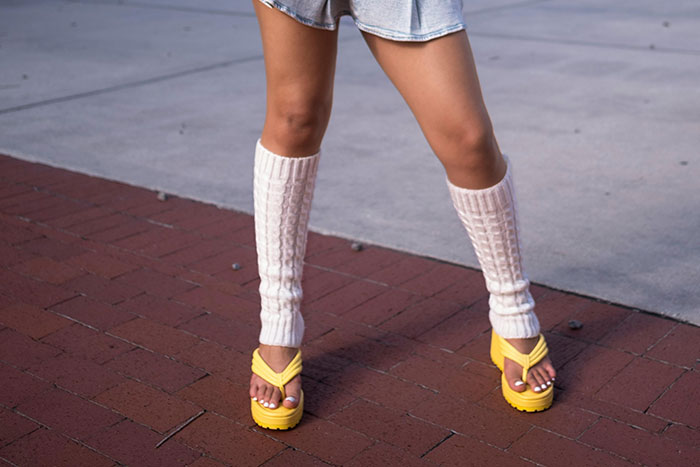 Person wearing yellow platform sandals and knit leg warmers, showcasing a retro fashion trend with stirrup pants.