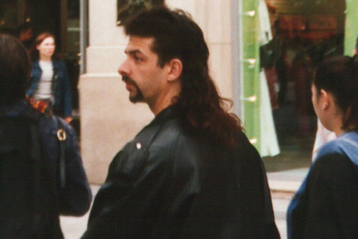 Man with a mullet hairstyle and leather jacket walking outdoors, reminiscent of past fashion trends including stirrup pants.