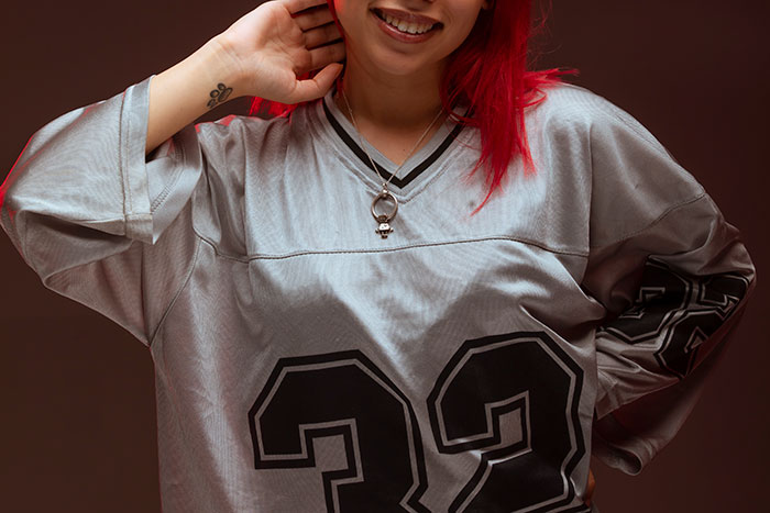 Person with red hair wearing a silver sports jersey with number 33, smiling and posing, representing stirrup pants fashion trends.