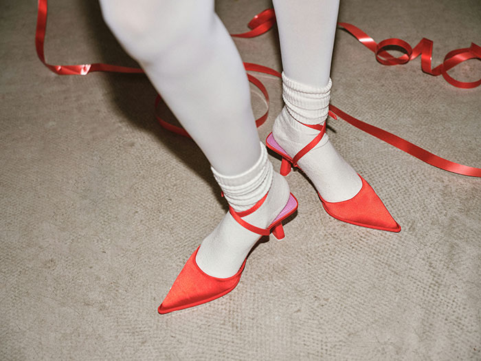 Person wearing stirrup pants with white socks and red heels on a carpeted floor with red ribbon around.