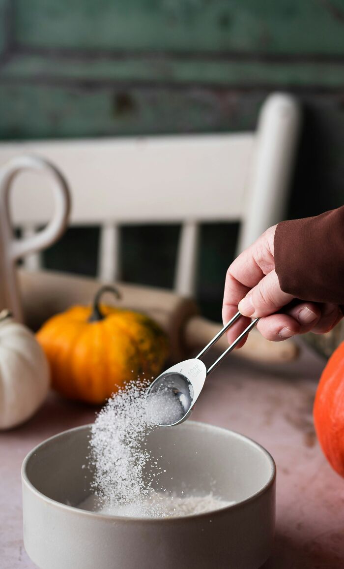 Hand pouring salt from measuring spoon into a bowl in a kitchen setting, highlighting mundane things that make people sick.