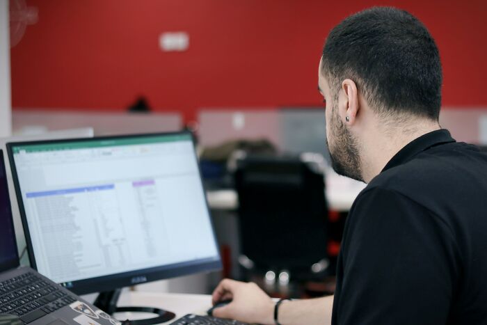 Tech guy fixing a customer's computer, focused on the screen in a modern office environment with red walls.