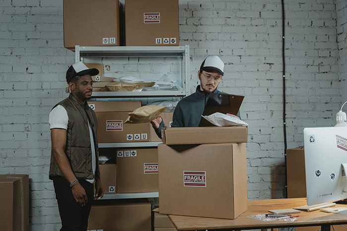 Two workers handling packages in a shipping area, illustrating the impact of a strict one minute late rule by the boss.