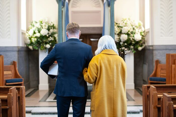 Man in a suit and woman in a yellow coat walking arm-in-arm in a decorated indoor venue, jaw-dropping moments concept.