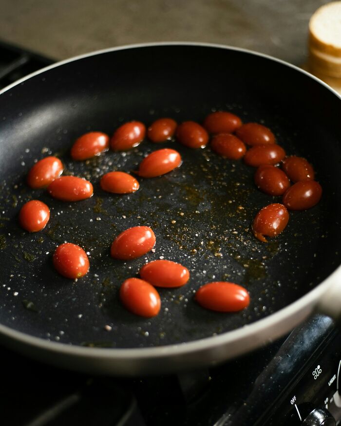 Cherry tomatoes sizzling in a frying pan with oil and spices, illustrating out-of-touch cooking moments recalled by people.