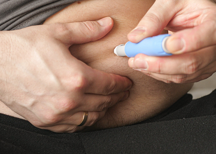 Person injecting themselves in the abdomen with a blue pen device related to Ozempic mouth weight-loss side effect concerns. Person injecting themselves in the abdomen with a blue pen device related to Ozempic mouth weight-loss side effect concerns.