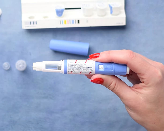 Hand holding an Ozempic injection pen with medical supplies on a blue surface highlighting weight-loss side effects. Hand holding an Ozempic injection pen with medical supplies on a blue surface highlighting weight-loss side effects.