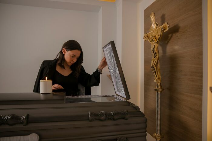 Woman in black standing by an open coffin with a candle, experiencing shocking moments people have lived through.