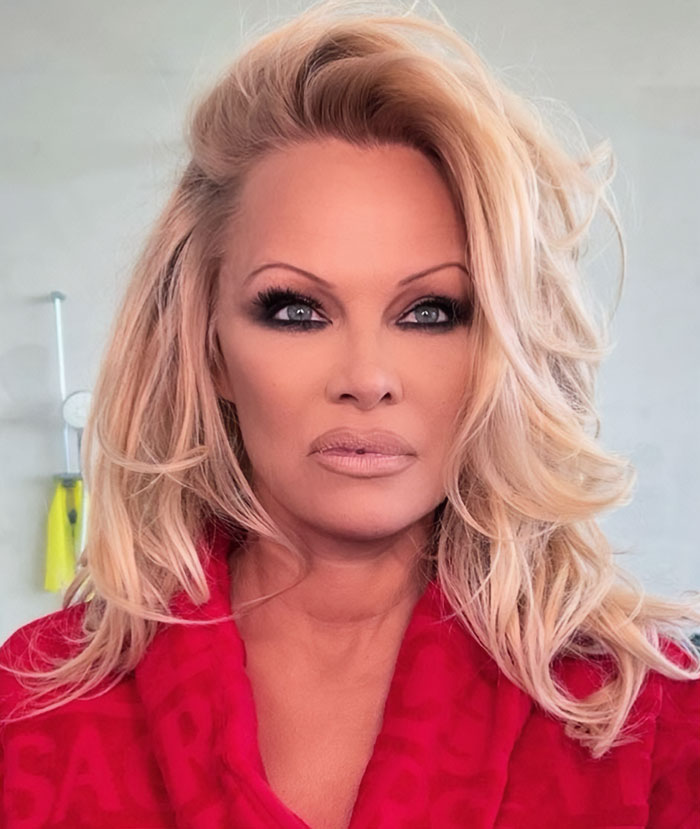 Pamela Anderson con estilo glamuroso de los 90, maquillaje de ojos audaz y cabello rubio voluminoso en bata roja. Pamela Anderson con estilo glamuroso de los 90, maquillaje de ojos audaz y cabello rubio voluminoso en bata roja.