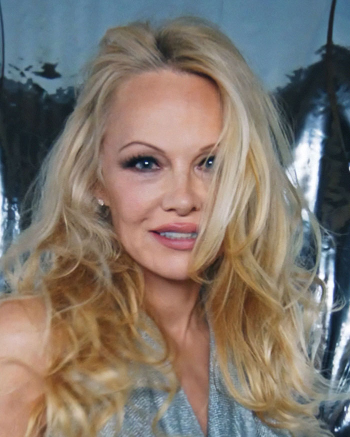 Pamela Anderson con look glamuroso de los 90, maquillaje llamativo y cabello rubio voluminoso en ambiente elegante. Pamela Anderson con look glamuroso de los 90, maquillaje llamativo y cabello rubio voluminoso en ambiente elegante.