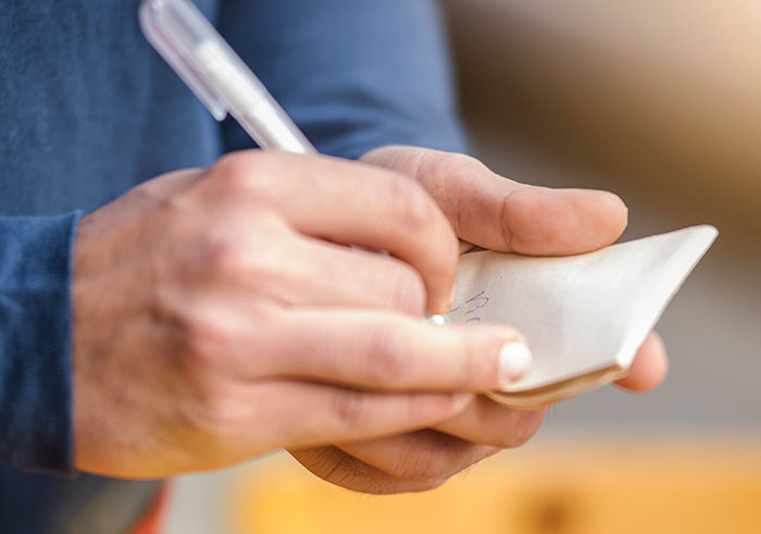Person writing a note on paper, illustrating resident leaving a nasty note on guest’s scooter incident. Person writing a note on paper, illustrating resident leaving a nasty note on guest’s scooter incident.