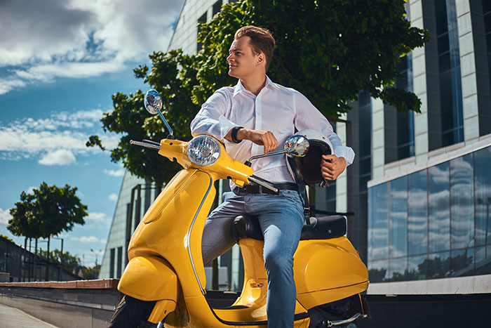 Young man sitting on a yellow scooter outdoors, holding a helmet, illustrating guest scooter and resident violations conflict. Young man sitting on a yellow scooter outdoors, holding a helmet, illustrating guest scooter and resident violations conflict.
