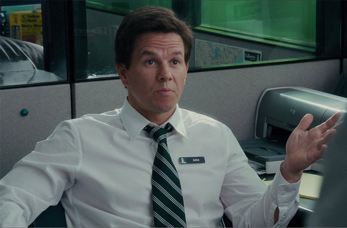 Actor wearing a white shirt and striped tie, portraying Steve Jobs in a film scene inside an office cubicle.