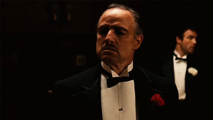 A man in a black tuxedo with a red rose, reflecting on legacy and public praise after passing.