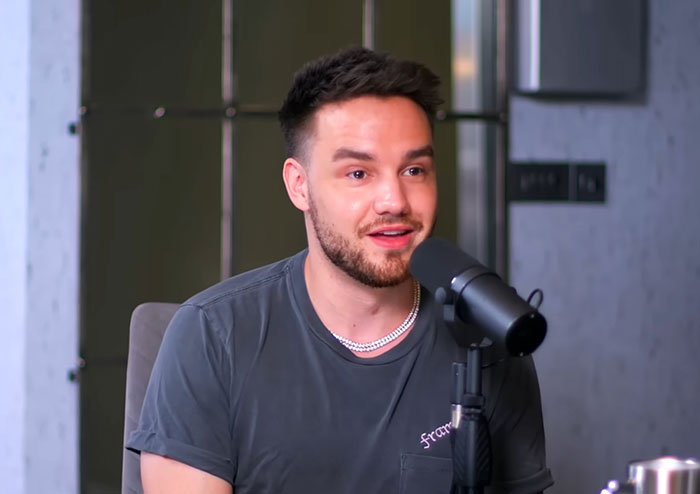 A young man with a beard speaking into a microphone during a podcast discussing Steve Jobs and celebrities.