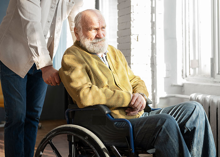Elderly man in wheelchair with caregiver nearby, reflecting on chilling final words doctors and nurses heard from patients.