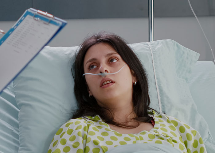 Young female patient in hospital bed with oxygen tube, nurses and doctors listening closely to chilling final words.