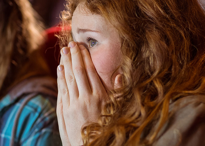 Woman with curly hair covering her mouth in shock, reacting to chilling final words heard by doctors and nurses.