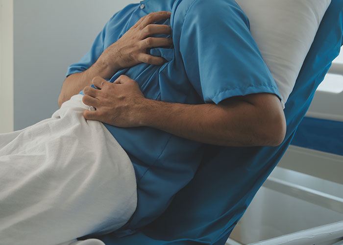 Patient in hospital gown clutching chest in bed, reflecting chilling final words doctors and nurses heard from patients.