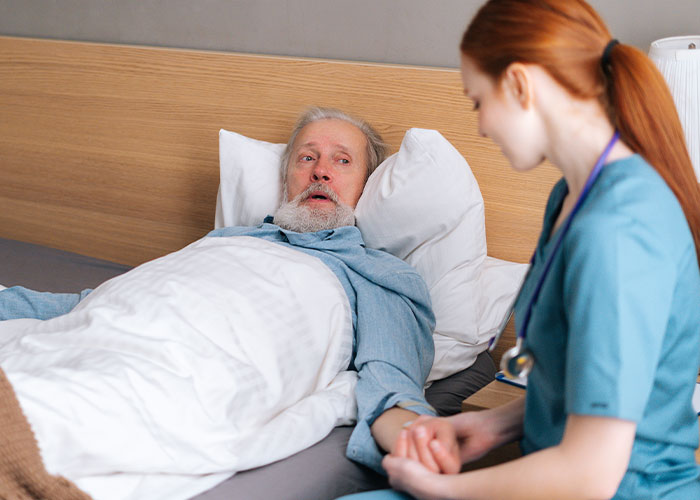 Elderly patient lying in bed holding hands with a nurse, depicting chilling final words doctors and nurses heard.