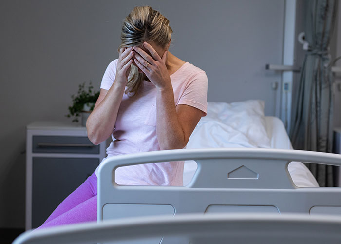 Woman in hospital room sitting on bed with head in hands, reflecting on chilling final words heard by doctors and nurses.