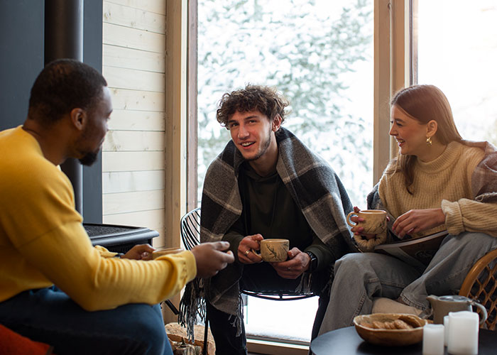 Three friends sharing warm drinks indoors near a snowy window, reflecting on chilling final words from dying patients.