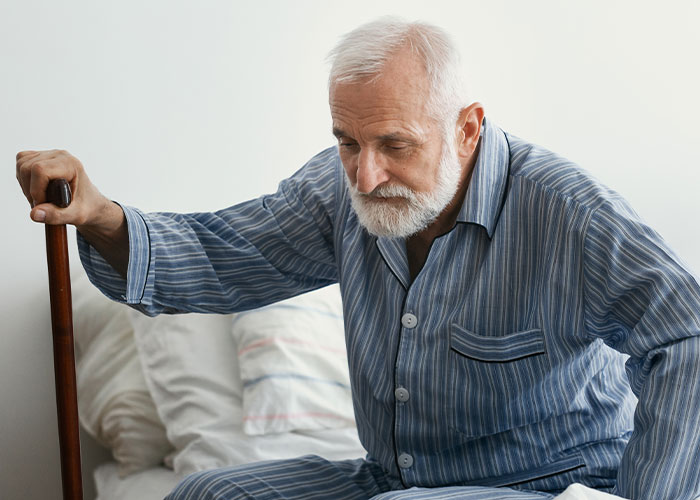 Elderly man in striped pajamas with a cane, sitting on bed, reflecting on final words doctors and nurses heard.