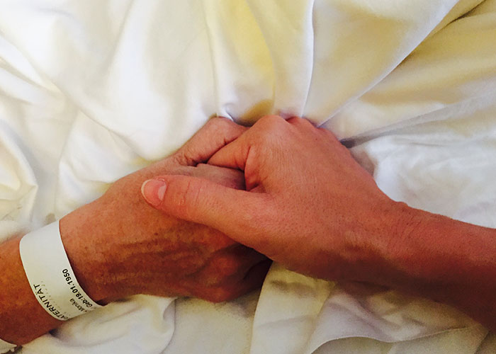 Two hands clasped on a hospital bed, symbolizing chilling final words from dying patients heard by doctors and nurses.