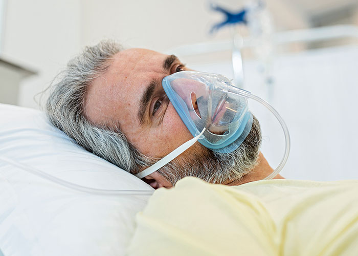 Middle-aged male patient lying in hospital bed with oxygen mask, highlighting dangers of patient lies in medical care.