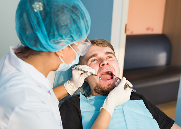 Dentist examining male patient’s mouth in clinic, highlighting risks when patient’s lie impacts medical care decisions.