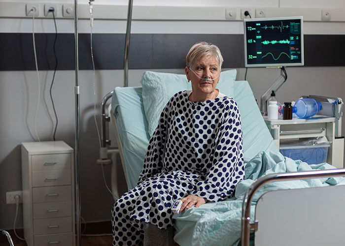 Older female patient in hospital bed with oxygen tube and vital signs monitor, highlighting risks of patient lies in healthcare.