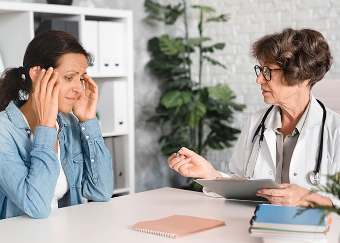 Patient in distress holding head while doctor discusses medical concerns during a critical healthcare consultation about patient lies.