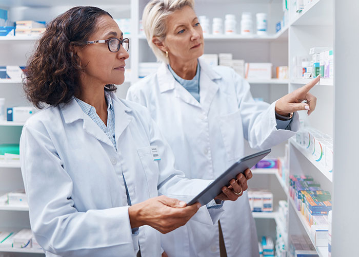 Two pharmacists in white coats reviewing medication shelves, highlighting risks when a patient’s lie nearly costs their life.