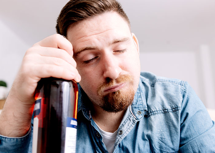 Man holding a bottle with eyes closed, representing a patient’s lie that nearly cost their life in a medical context.