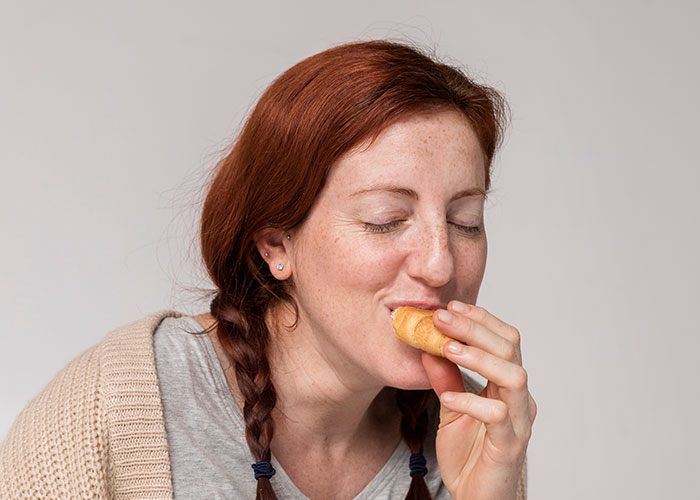 Red-haired woman with braided hair eating a small pastry, illustrating patient’s lie impact on health risks.