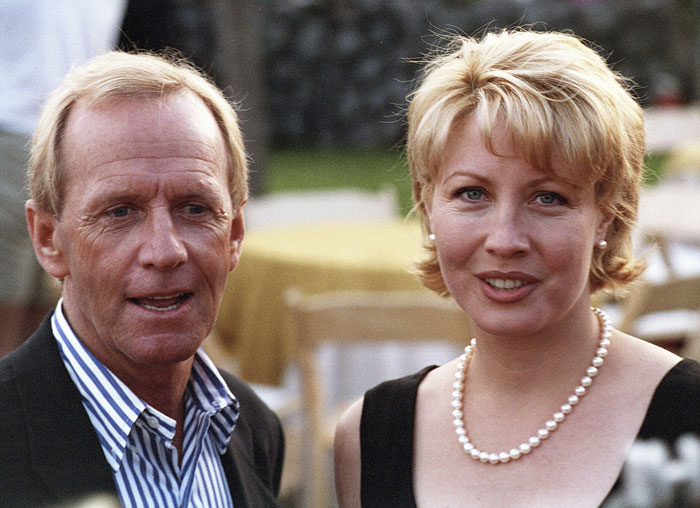 Paul Hogan, legendary Crocodile Dundee star, pictured with a woman at an outdoor event, smiling and dressed formally.
