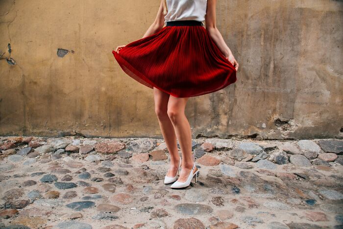 Woman in a red skirt and white heels standing on cobblestone street, representing questions women would ask men without judgment.