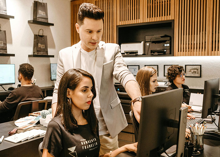 Boss telling workers their pay is late while showing off his new truck in a modern office setting with employees at computers