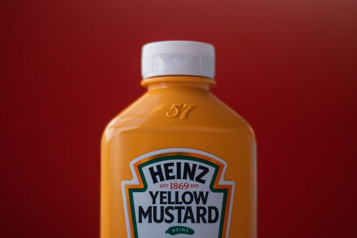 Plastic bottle of Heinz yellow mustard against a red background, illustrating common foods that go bad quickly.