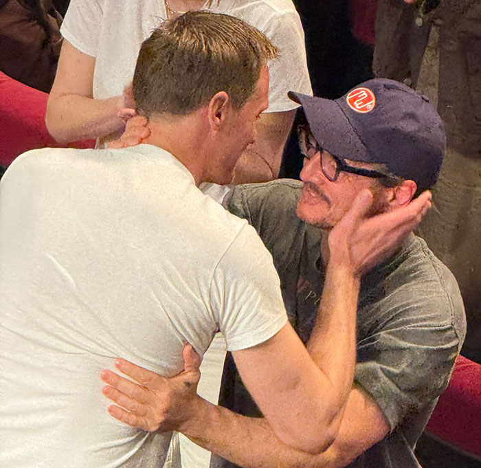 Two men embracing warmly in a crowded room, related to Harry Potter star in x-rated gay film and standing ovation.
