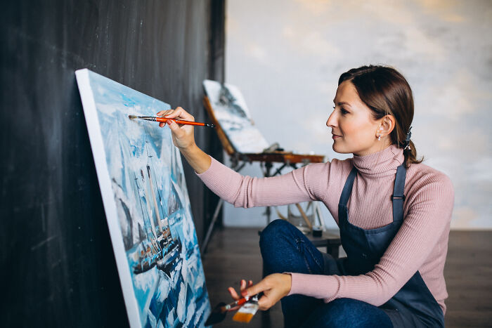 Woman painting a canvas in a studio, illustrating the concept of folks romanticizing experiences they have not really had.