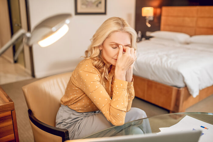 Woman stressed and overwhelmed in a bedroom setting experiencing feelings that folks only romanticize because they have not really experienced them