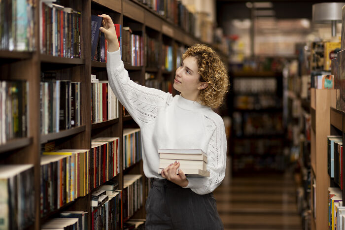 Young woman in a library selecting books, representing things folks only romanticize without truly experiencing them.