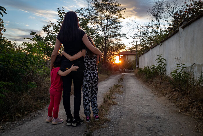 Woman and children embracing on a rural path at sunset, illustrating things folks only romanticize without real experience.