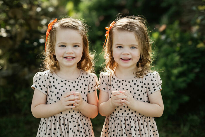 Two young girls with curly hair and polka dot dresses smiling outdoors, illustrating things folks romanticize.