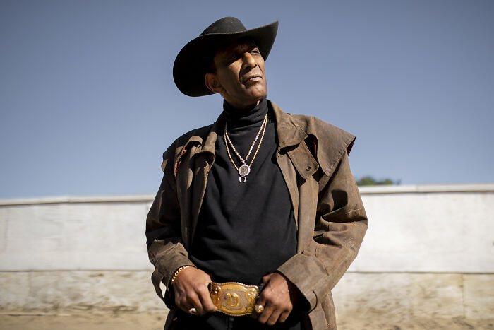 Man in cowboy hat and brown jacket standing outdoors, symbolizing romanticized adventurous experiences.