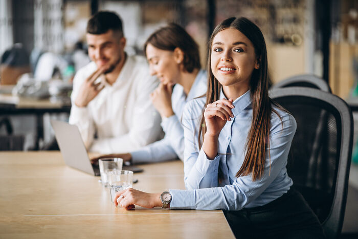 Young woman smiling confidently at a work meeting, highlighting folks who romanticize experiences they haven’t lived.