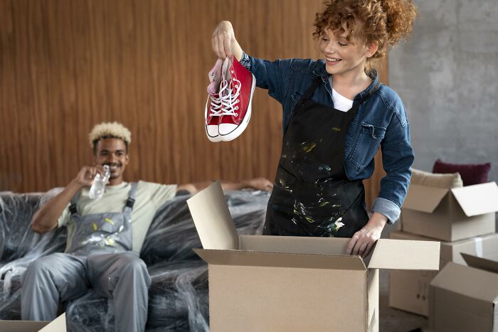 Young couple experiencing moving day, unpacking boxes and holding sneakers, showing moments people only romanticize.