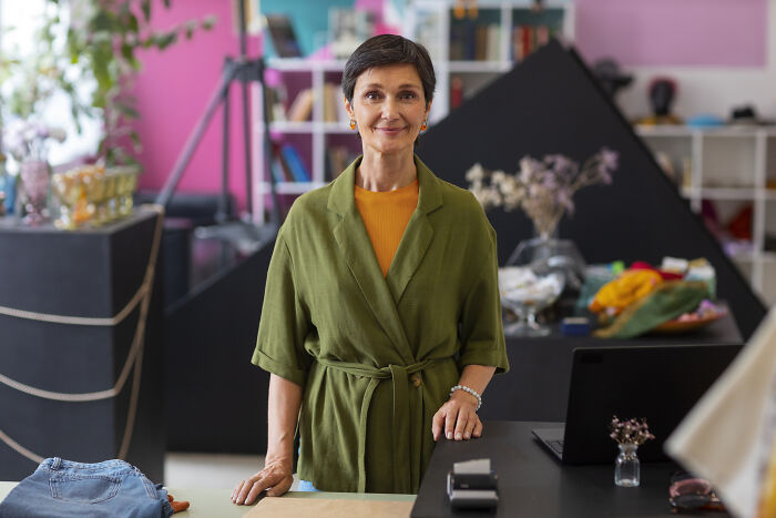 Middle-aged woman in green robe standing in a cozy room, symbolizing things folks only romanticize without experience.